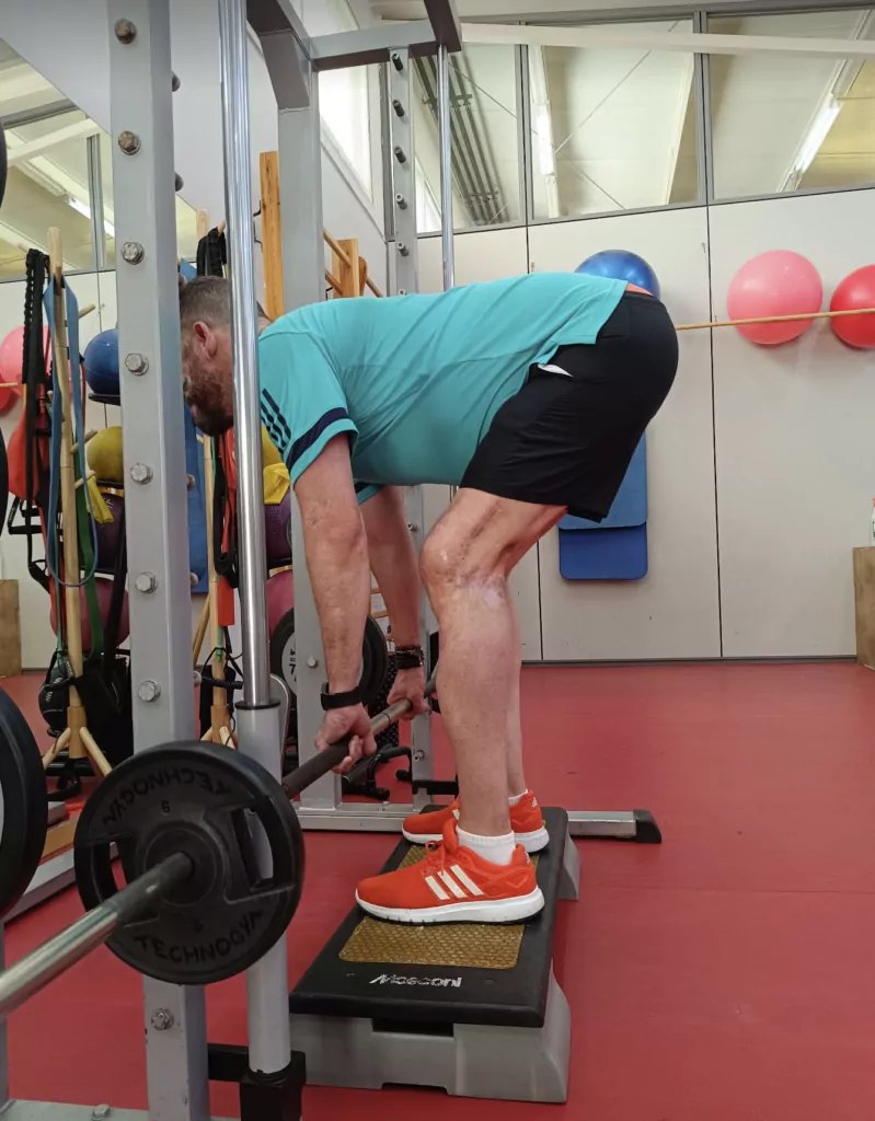 Paciente realizando peso muerto con barra en el gimnasio durante una sesión de readaptación deportiva